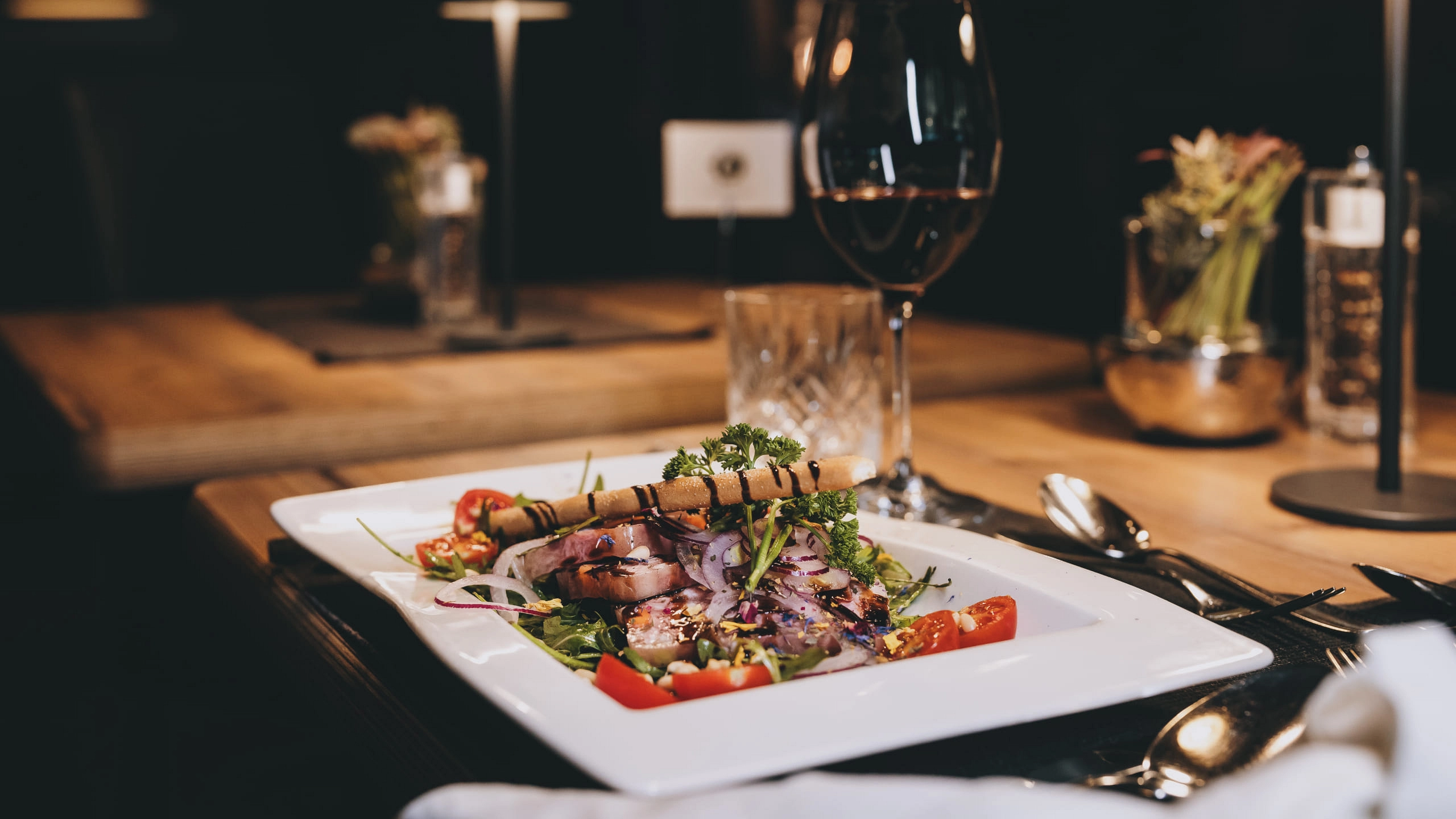 Ein Gourmetgericht auf einem weißen Teller mit Gemüse und Wein im Hintergrund