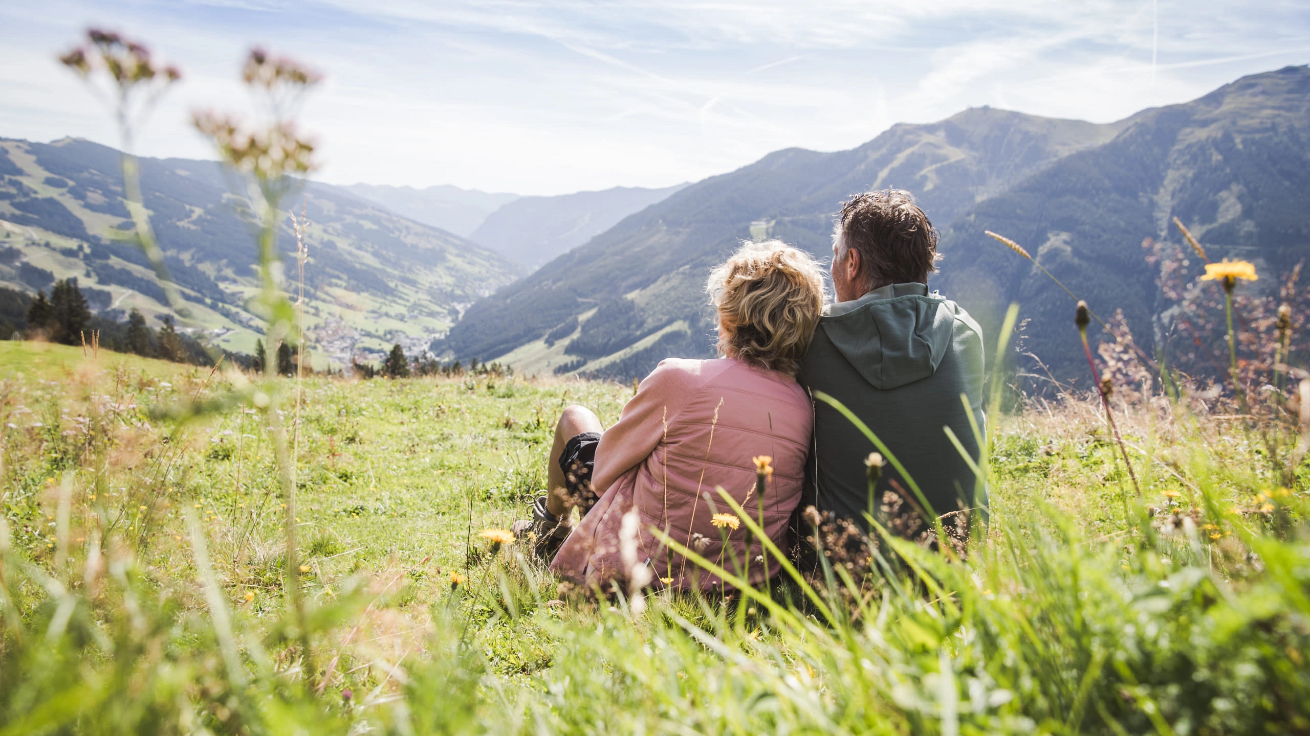 Paar sitzt auf einer Wiese in den Bergen von Saalbach Hinterglemm