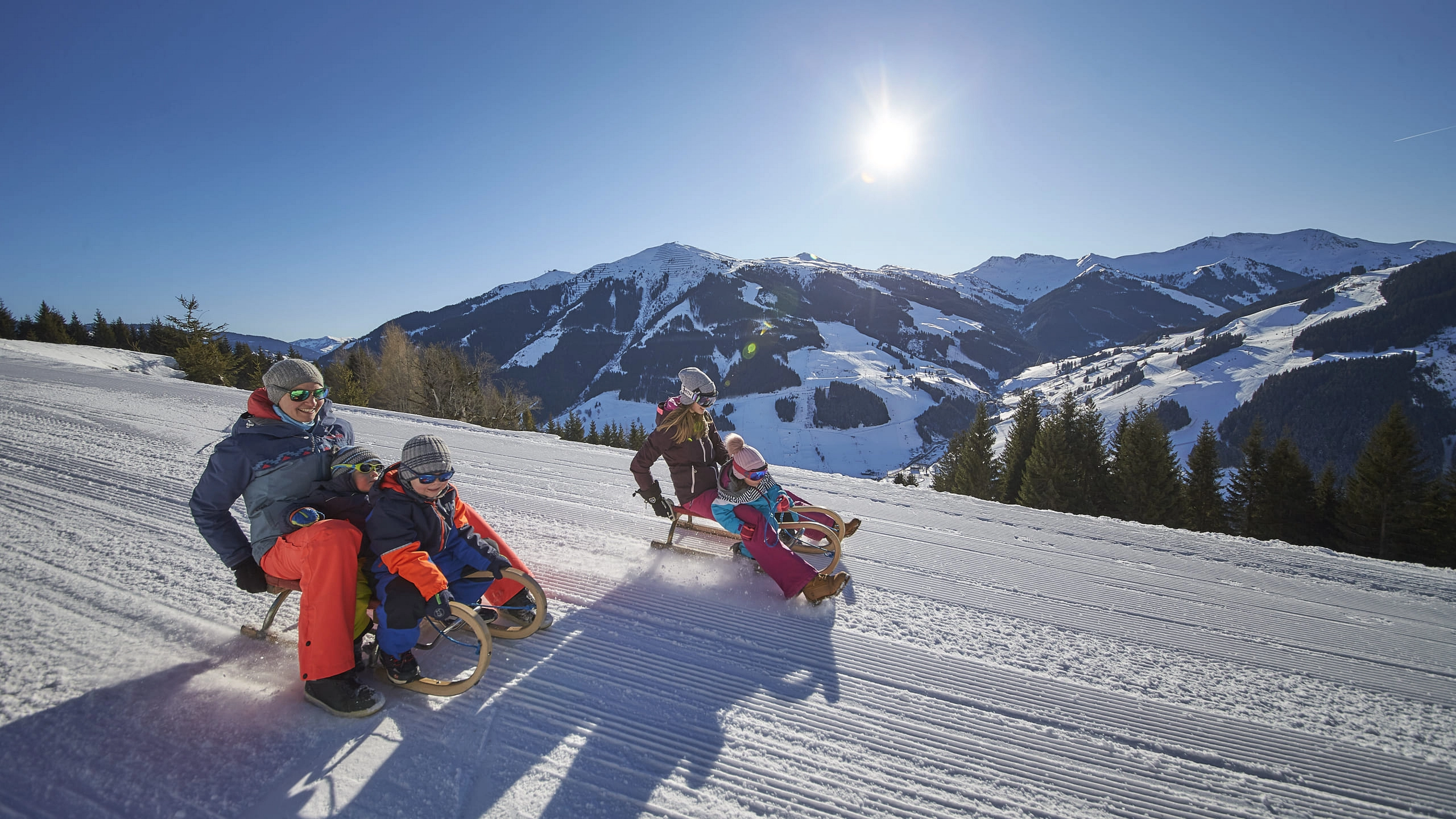 Menschen rodeln auf einer verschneiten Piste mit Bergen im Hintergrund