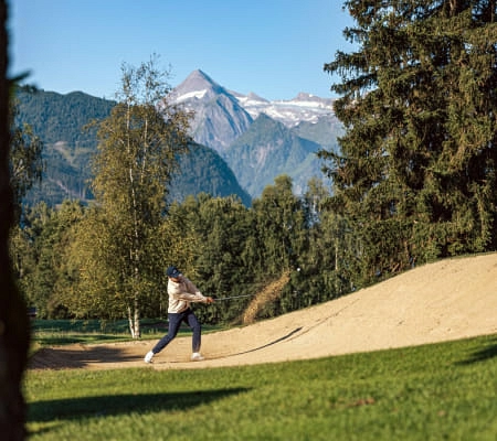 Golfspieler schlägt aus dem Sandbunker mit Bergen im Hintergrund