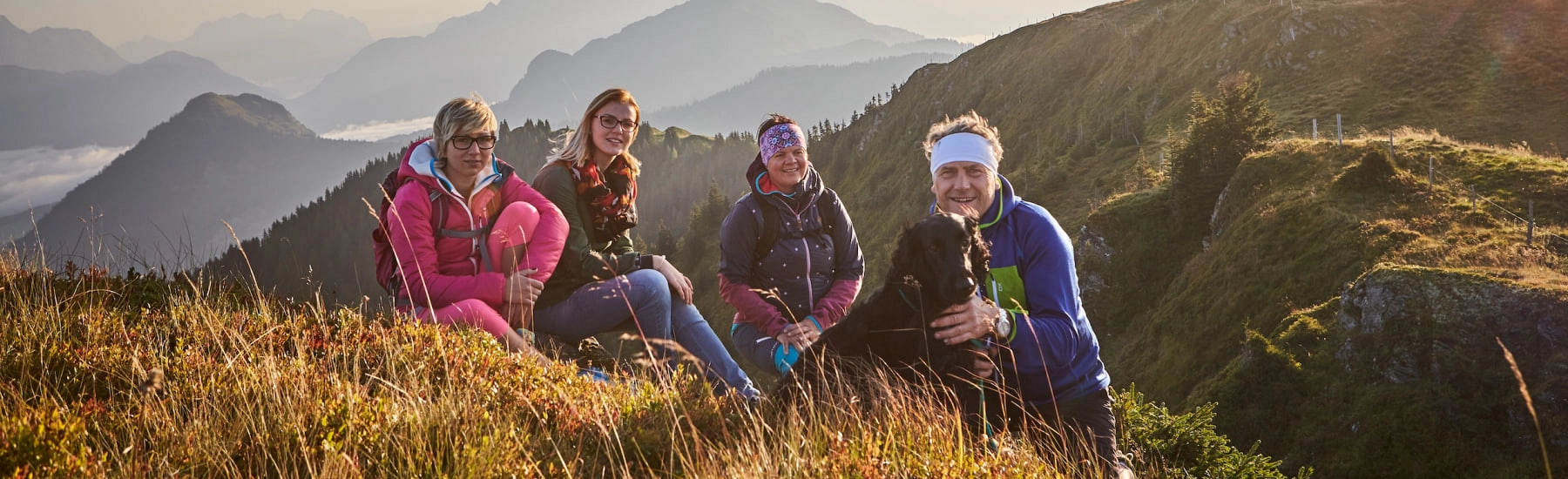Eine Gruppe von vier Frauen sitzt auf einem grasigen Hügel mit Bergen im Hintergrund
