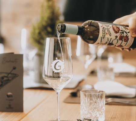 Weißwein wird in ein Glas mit Logo gegossen.